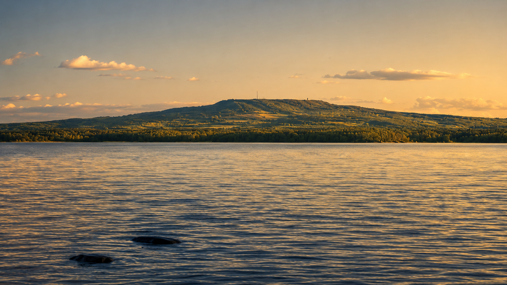 En stilla strandlinje i skymning där mörkt vatten möter land och vid himmel