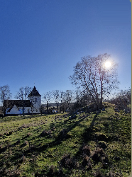 Adelsö kyrka intill Kungshögarna i motljus vid Mälaren